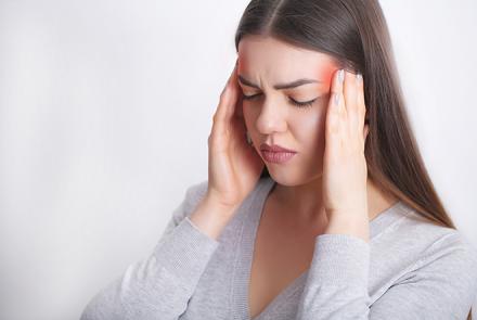 A stock pic of a woman with long hair holding her throbbing temples signifying migraine pain