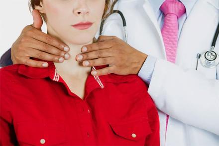 A stock image of a doctor examining the thyroid of a woman