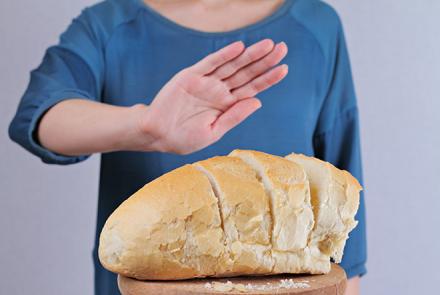 A person in a blue shirt with head cut off holding hand up to say no to a loaf of bread