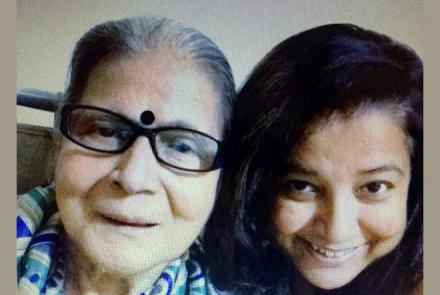 Mausumi, a dark haired woman on the right with her mother, a person with dementia on the left. Mother is wearing specs and  a bindi on her forehead and you can see the blue and white sari draped around her shoulders
