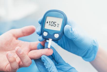 A person with blue gloves pricking a person's finger using a blood glucose monitor