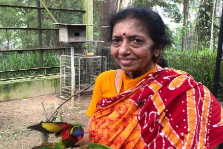 The author, a woman in a red and yellow sari and a yellow blouse, holding birds