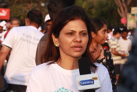 A young woman in the foreground in a white t-shirt talking into a mic