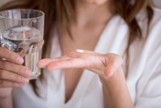 A woman whose head is not visible holding a pill in her palm and a glass of water