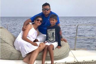 Pooja in a white dress with  her son and husband on the deck of a ship