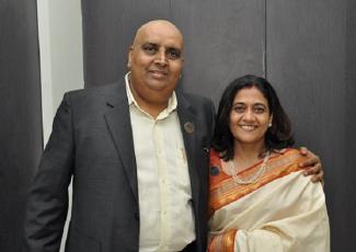 Dilip lives with multiple myeloma and is in a white shirt and black jacket with his wife in a white and red sari