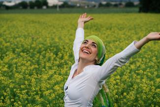 Stock image of a woman in a white shirt celebrating in a green field with a new look with a scarf to address hair loss during chemotherapy