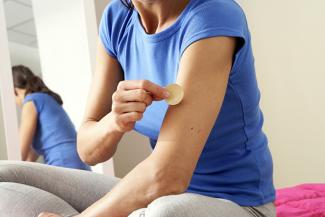 Stock pic of a woman in blue top and grey slacks applying a nicotine replacement patch
