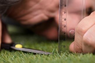 A person measuring the length of grass blades with a ruler and trimming the grass