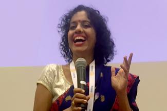 Urmila Prabhu speaking at a Vitiligo forum with a black sari and golden blouse 