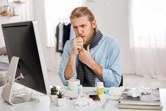 Image: Man at a work desk coughing with some medicine on the desk