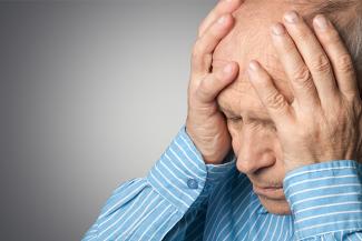A person in a blue full sleeved shirt holding his head indicating a brain stroke 