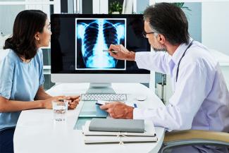 A doctor on the right with a stethoscope and a woman on the left looking at a scan of lungs. 