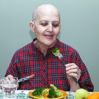 A cancer patient, shown as bald due to chemotherapy eating food