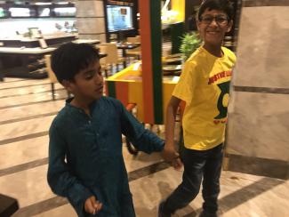 A young boy in a blue kurta walking hand in hand with his friend in yellow t-shirt and jeans in a hotel lobby