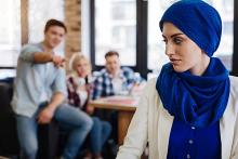 Stock image of a woman in blue scarf in the foreground and a group of people in the background pointing to her