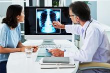 A doctor on the right with a stethoscope and a woman on the left looking at a scan of lungs.