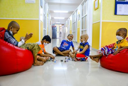 Children going through cancer treatment, wearing face mask and bald head sitting in red bean bags, playing together