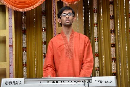 Image: Adithya Venkatesh, autistic music prodigy in a red kurta on stage playing Carnatic music on his keyboard