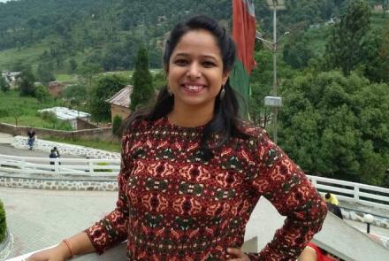 Aditi who has Fibromyalgia in an outdoor balcony setting in a red printed full sleeved dress 