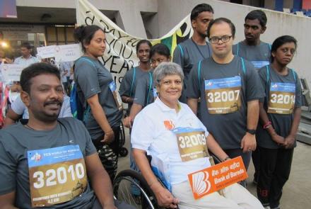 Jacqueline Colaco on a wheel chair, in white at the TCS 10K with some of the other participants