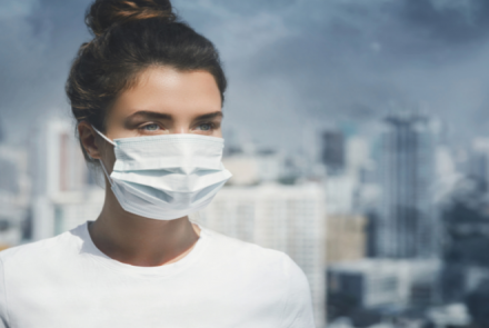 Poor air quality in an urban city and a woman wearing a surgical mask