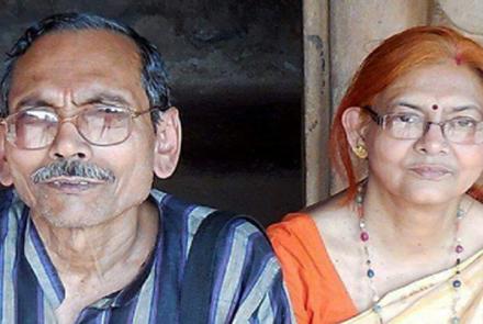An elderly and spectacled couple Mr Pranab Basu in a blue striped shirt with his wife in an orange blouse and a cream sari