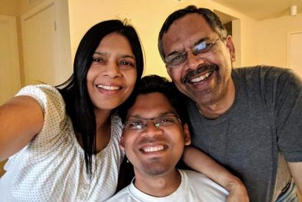 Image description: Pratyush a young dark haired Indian man in a white t-shirt in the centre with his mom on the left in a white top taking the selfie and his spectacled father on the right in a grey shirt 