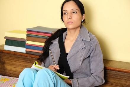 Image: Stock pic of a woman wearing a grey jacket, light blue pants staring in front with nooks lined up behind her