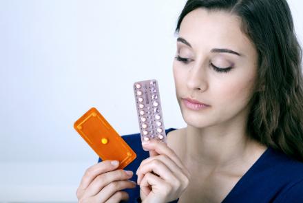 Image shows a woman looking at a strip of medicines