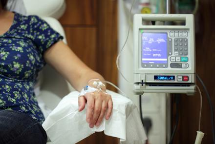 Image: A woman's left arm is visible, attached to a diagnostic machine in a hospital setting  