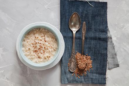 A pic of a bowl of oats porridge with spoons on the right with flax seeds spilling over 