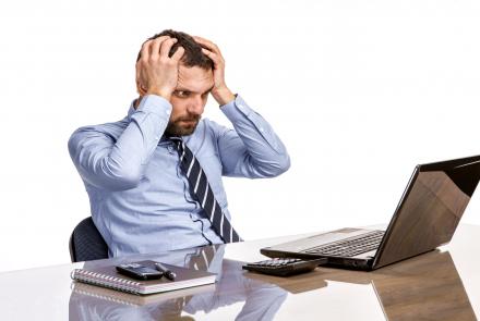 A person clasping head in pain and looking at a laptop 