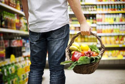 Back of a person carrying a basket of fruits and vegetables in the shopping aisle 