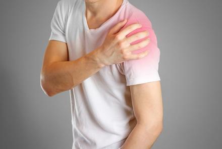 A person in a white t-shirt holding his shoulder and signalling pain 