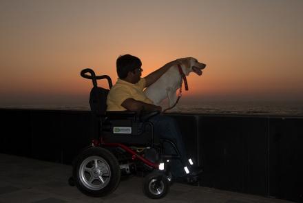 Karan in his wheelchair due to SMA III and his labrador angel looking out into a glorious sunset