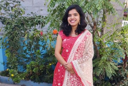 A woman in a red kurta and white dupatta standing in a garden