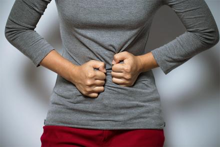 A woman in a grey top and red pant clutching her stomach in pain 