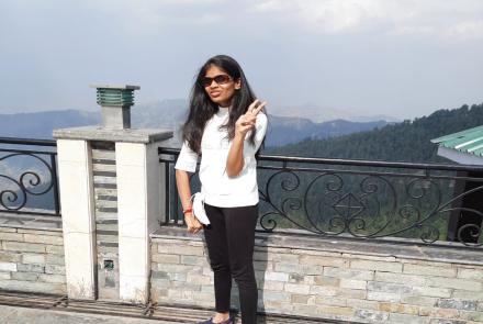 A young lady in a white shirt and black pants standing on a hilly road. She has a genetic and rare autosomal disorder Benign Hereditary Chorea