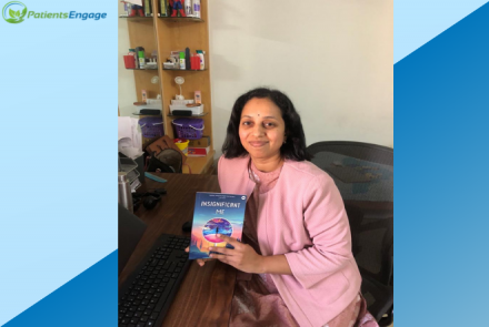 The author Dr Prathima holding her book in her hand. She is wearing a bit jacket and is seated on a sofa