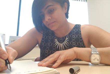 Image of Ekta, in a black dress, short black hair journaling as part of her self care routine