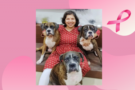 A woman in a red kurta and white pants sitting with 3 dogs 