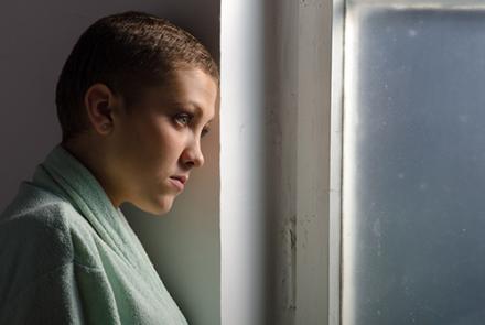Stock pic of a cancer patient with no hair looking out of a window for this article on managing side-effects of chemotherapy