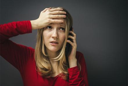 A woman in a red dress on the phone and holding her head in distress 
