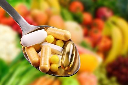 Supplement capsules in a spoon in sharp focus against soft focus of vegetables and fruits