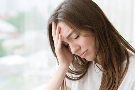 Image: Stock pic of woman with brunette hair holding her head during a migraine attack