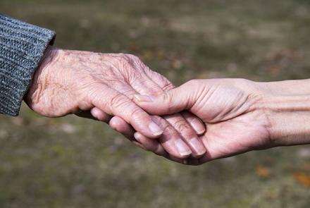 Image indicates a caregiver holding the hand of an older person