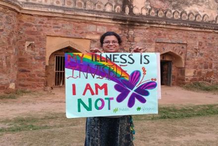 Image: A woman stands with a poster showing her support for fibro warriors