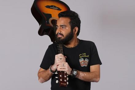A man with a beard in a black t-shirt holding a guitar that clearly shows his hands with white pigmentation