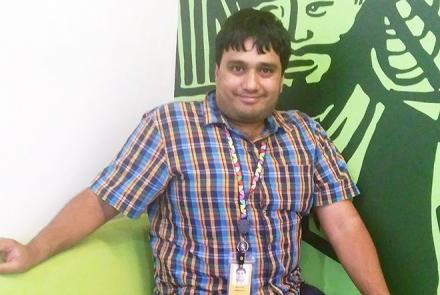 Image: Anirudh, autistic young man sitting in a checked shirt and sitting on a green sofa and a green background